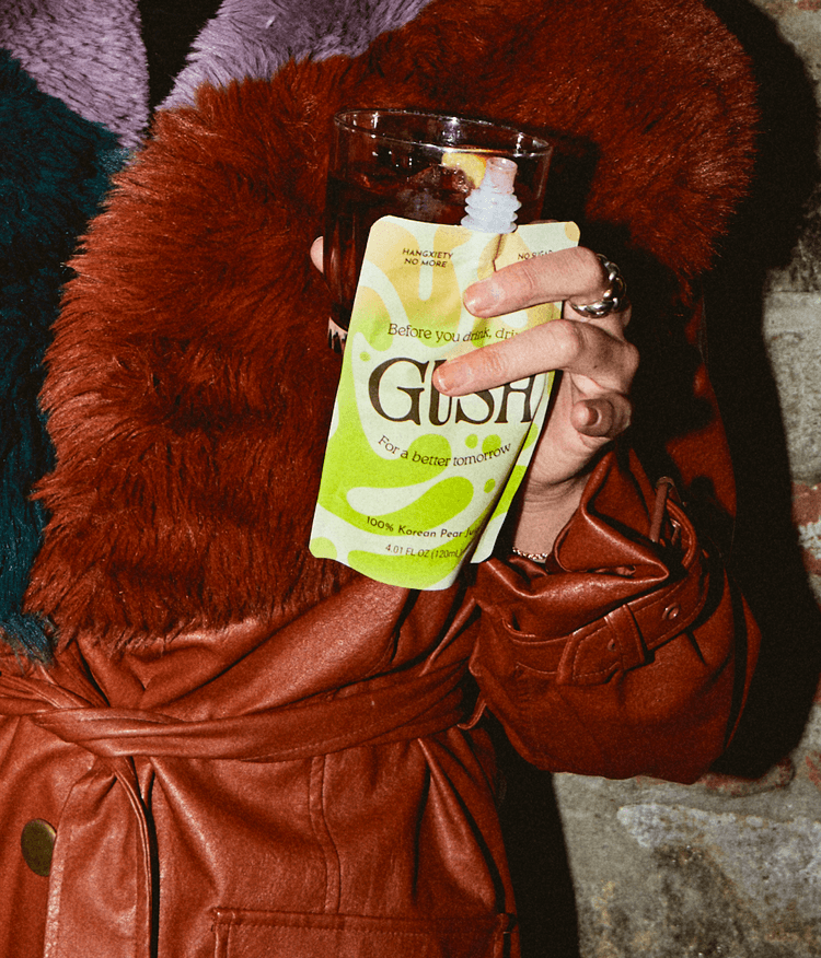 Close up photo of a person in a dark red jacket holding a Gush drink pouch.